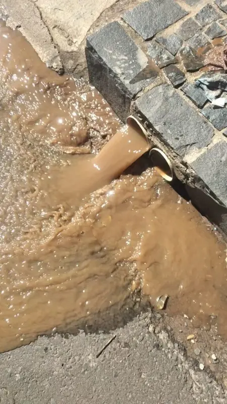 Água barrenta saindo de tubulação de drenagem pluvial em calçada
